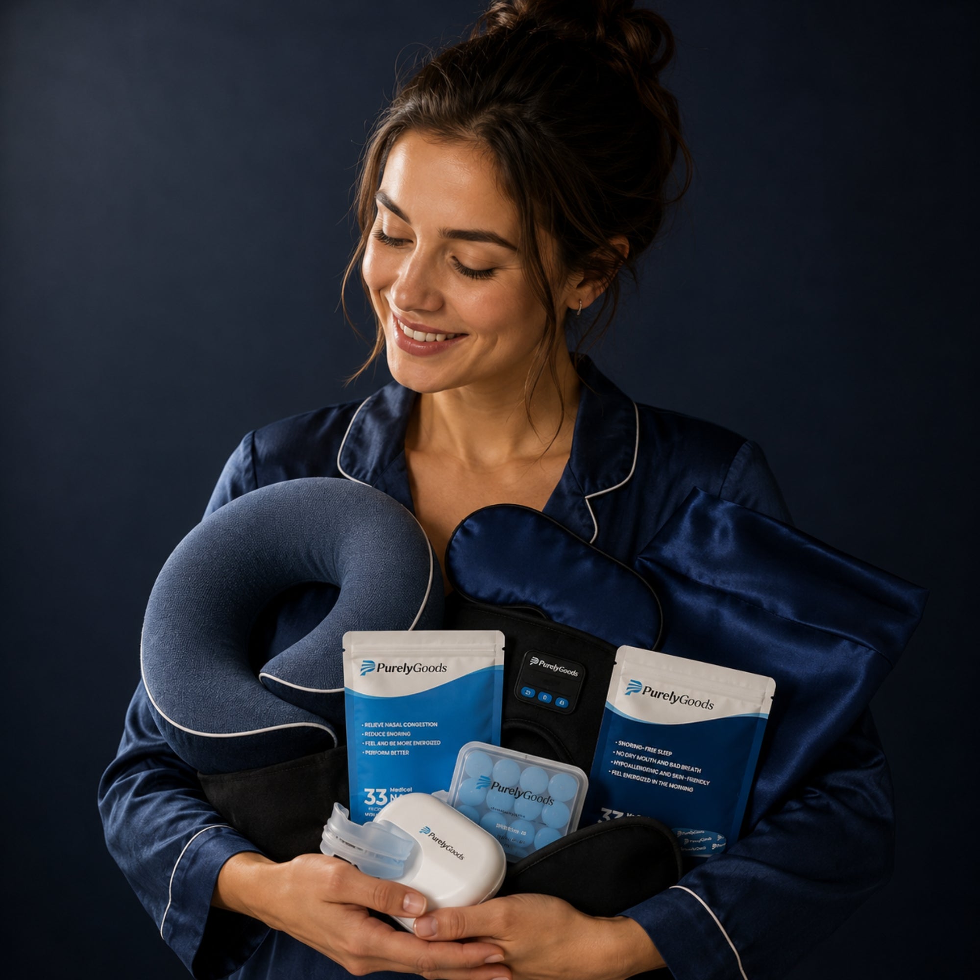 Vrouw in donkerblauwe satijnen pyjama houdt een bundel slaapproducten vast met nekkussen, oogmasker en PurelyGoods slaapaccessoires.