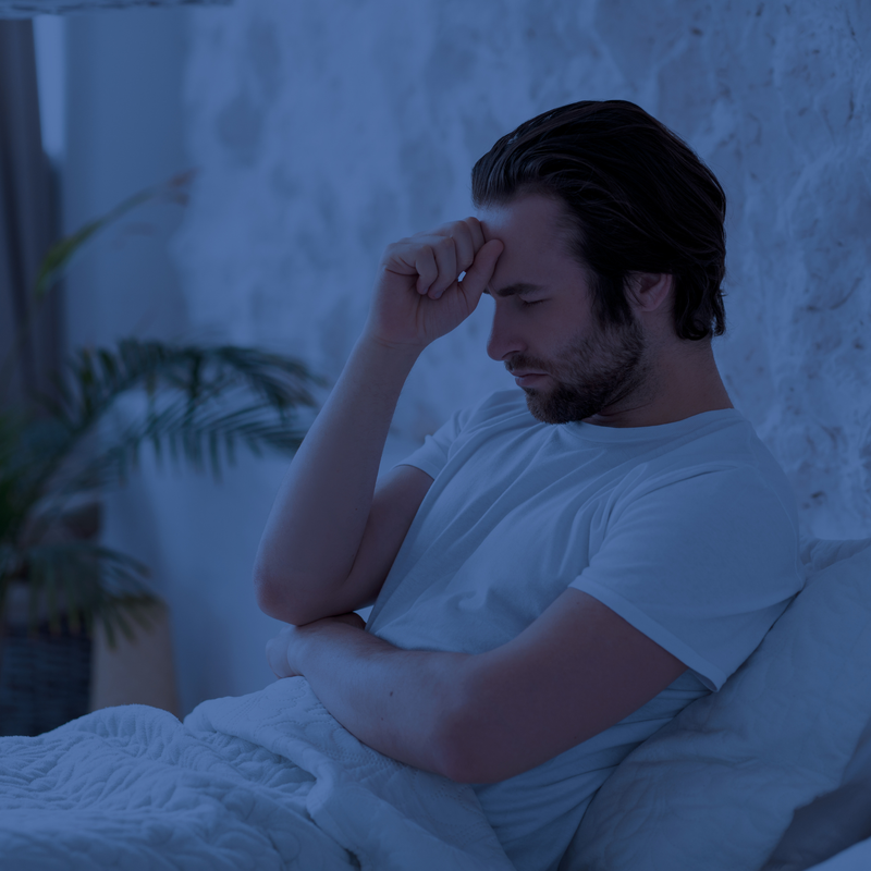 Man zit in bed met hand op voorhoofd door stress en slaapproblemen